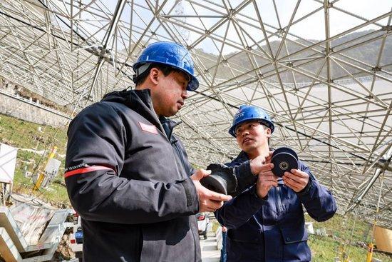 2023年2月13日，姜鹏（左）在贵州“中国天眼”的反射面板下与工作人员交谈（维护保养期间拍摄）。新华社记者 欧东衢 摄